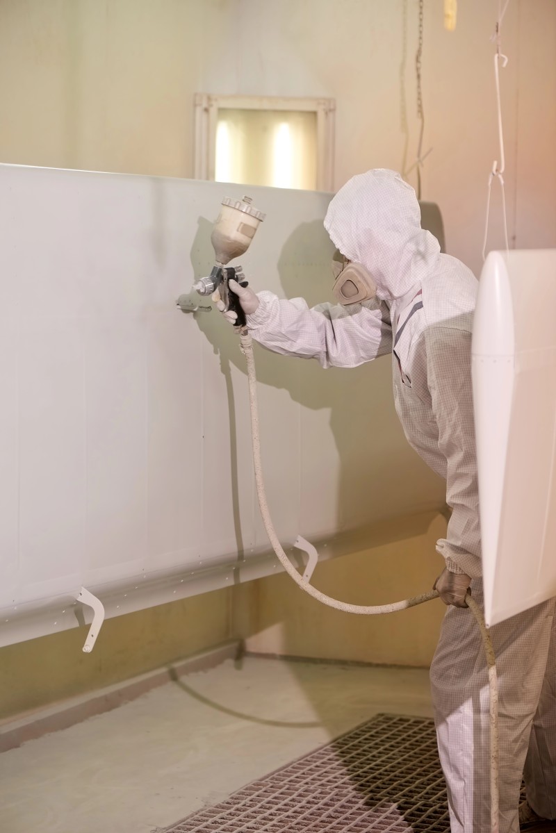Worker spray painting airplane wing.